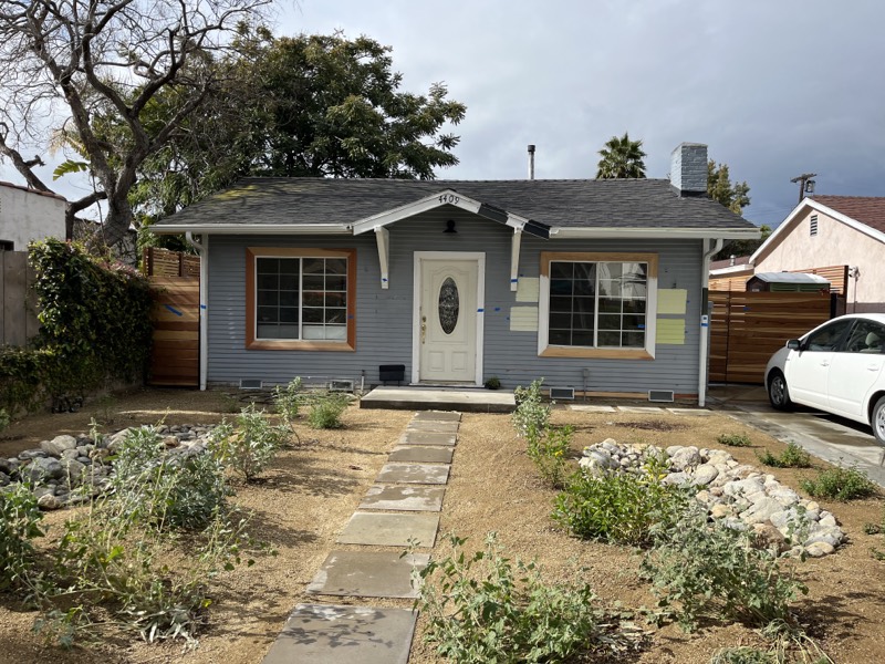 The freshly painted house with a new flagstone path and small young plants set out in bare soil.