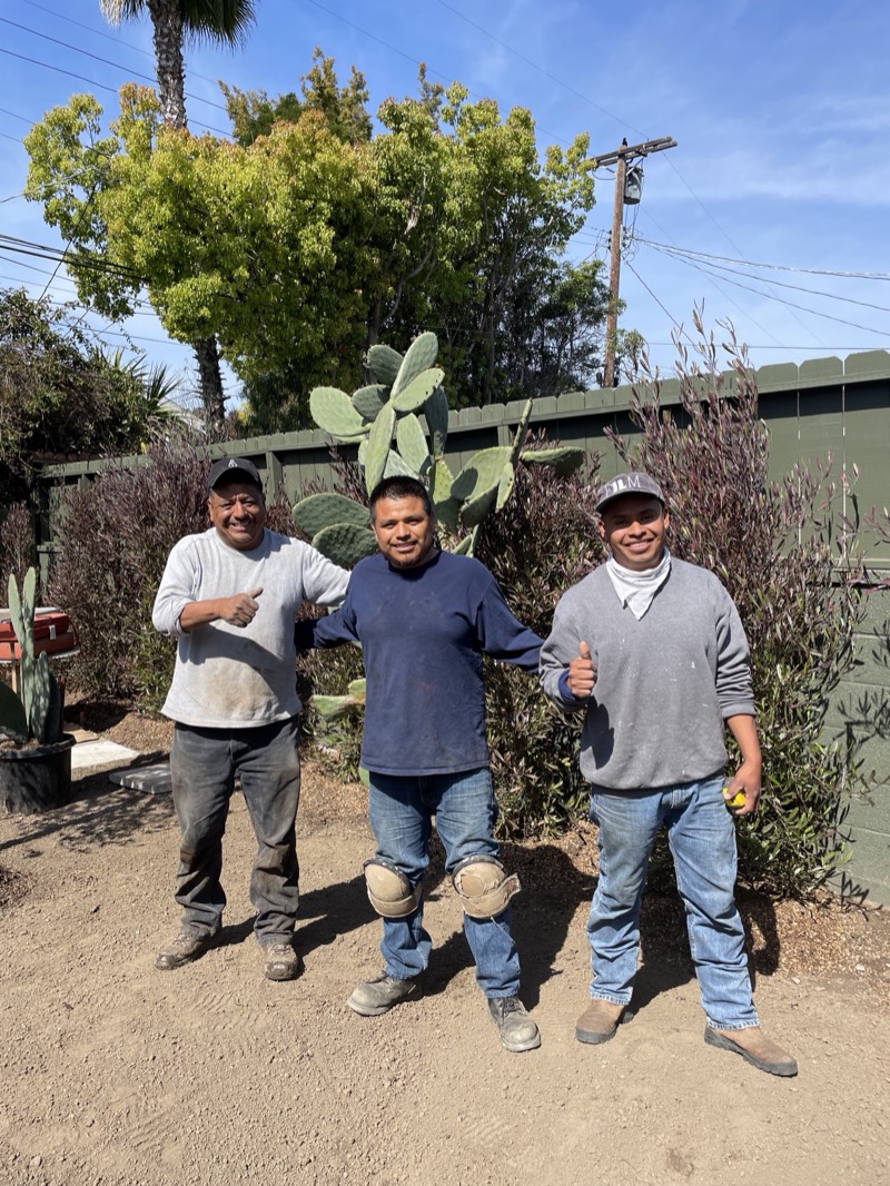 Three members of the crew giving a thumbs up in the back yard beside a prickly pear.